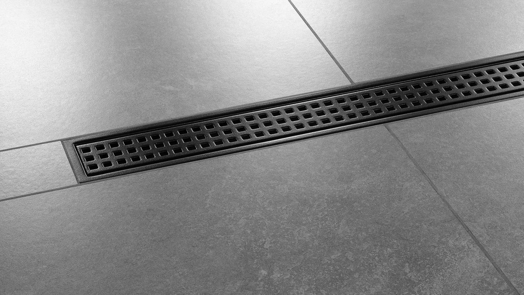Gros plan sur un sol de douche avec carrelage de couleur gris fonc&eacute; et caniveau Schl&uuml;ter-KERDI-LINE-B install&eacute; au centre de la douche, design SQUARE, finition TRENDLINE, noir graphite mat.