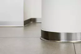 Vloer met plinten van geborsteld aluminium rondom een witte kolom en langs een witte wand