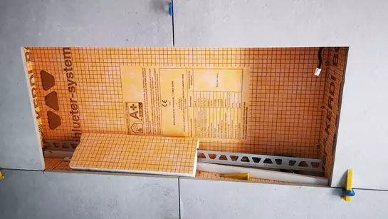 Pohled na šedou obloženou stěnu, ve kter&eacute; je vestavěna osvětlen&aacute; nika KERDI-BOARD-NLT.