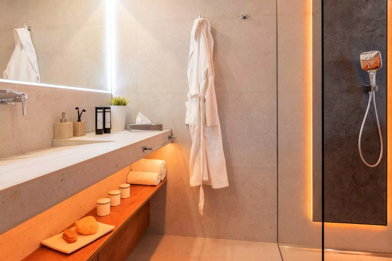 Warm beleuchtetes Bad mit verglaster Dusche, gro&szlig;em Waschbecken, Spiegel und Holzablagen
