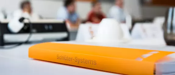 Een oranje ordner met het opschrift Schl&uuml;ter-Systems ligt op een tafel