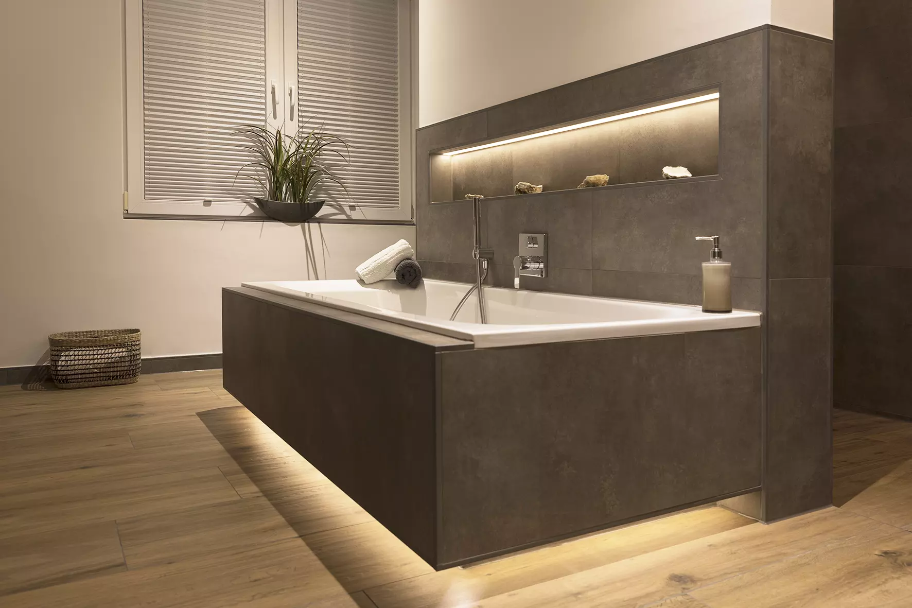 Eine Badewanne mit beige gefliestem Wannenk&ouml;rper scheint zu schweben aufgrund von nach innen versetzter Sockelbeleuchtung