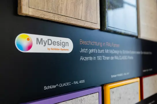 Wand mit Profilen in unterschiedlichen Farben, mit individueller Bedruckung und Informationen zu MyDesign.