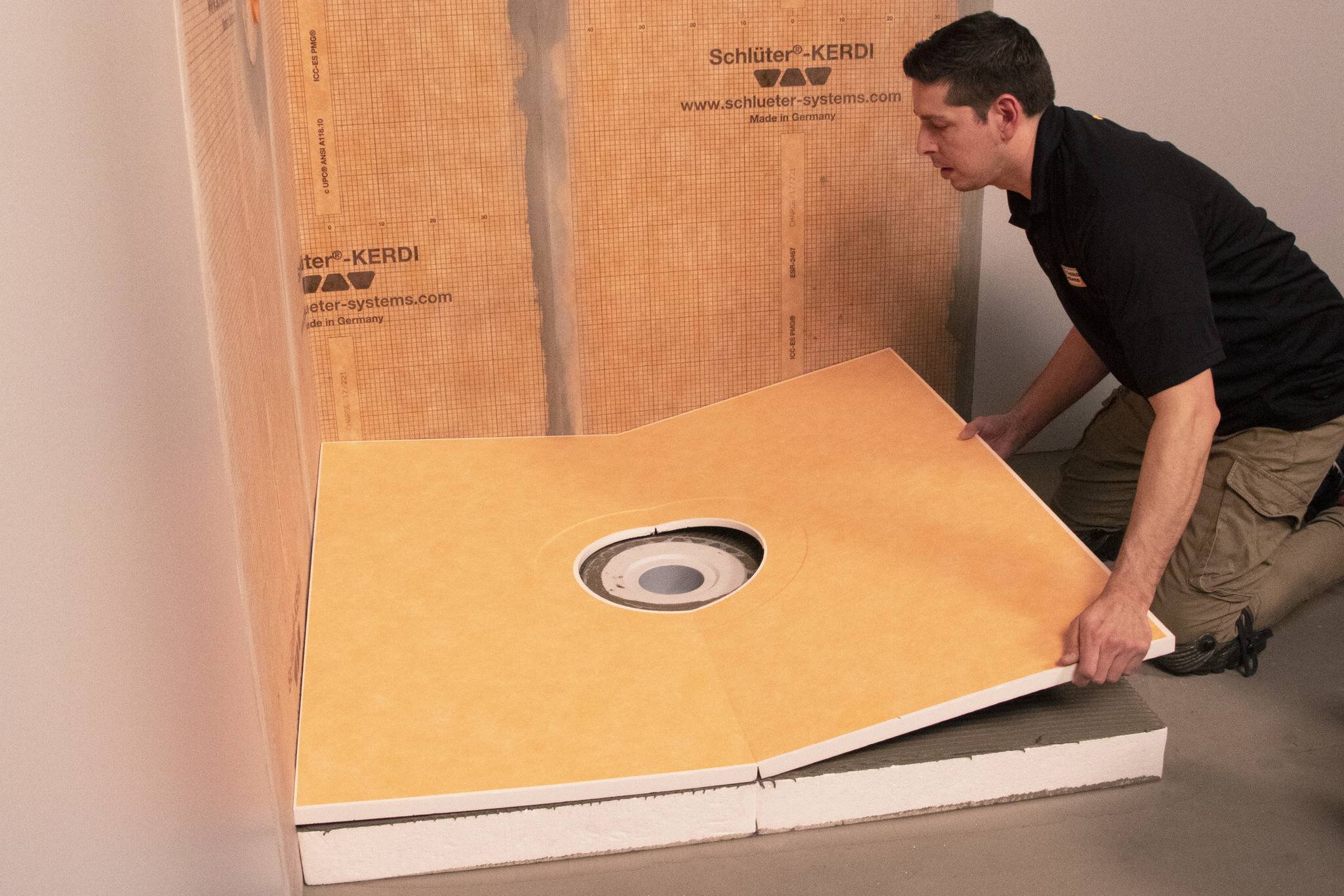 Un homme installe un bac de douche orange sur la plaque de compensation KERDI-SHOWER-CB.