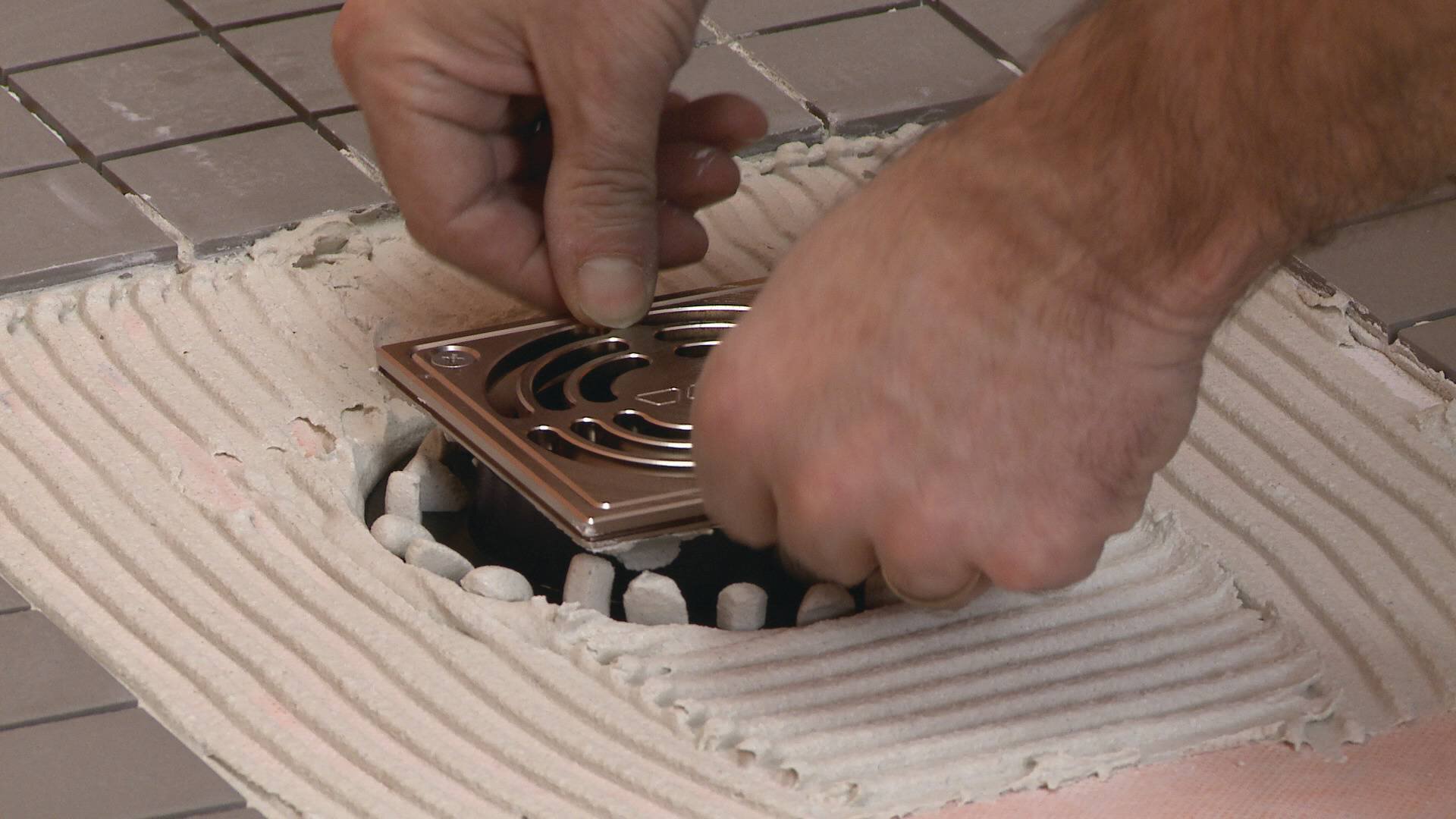 Un installateur fixe une grille de drain dans une bride recouverte de mortier-colle.