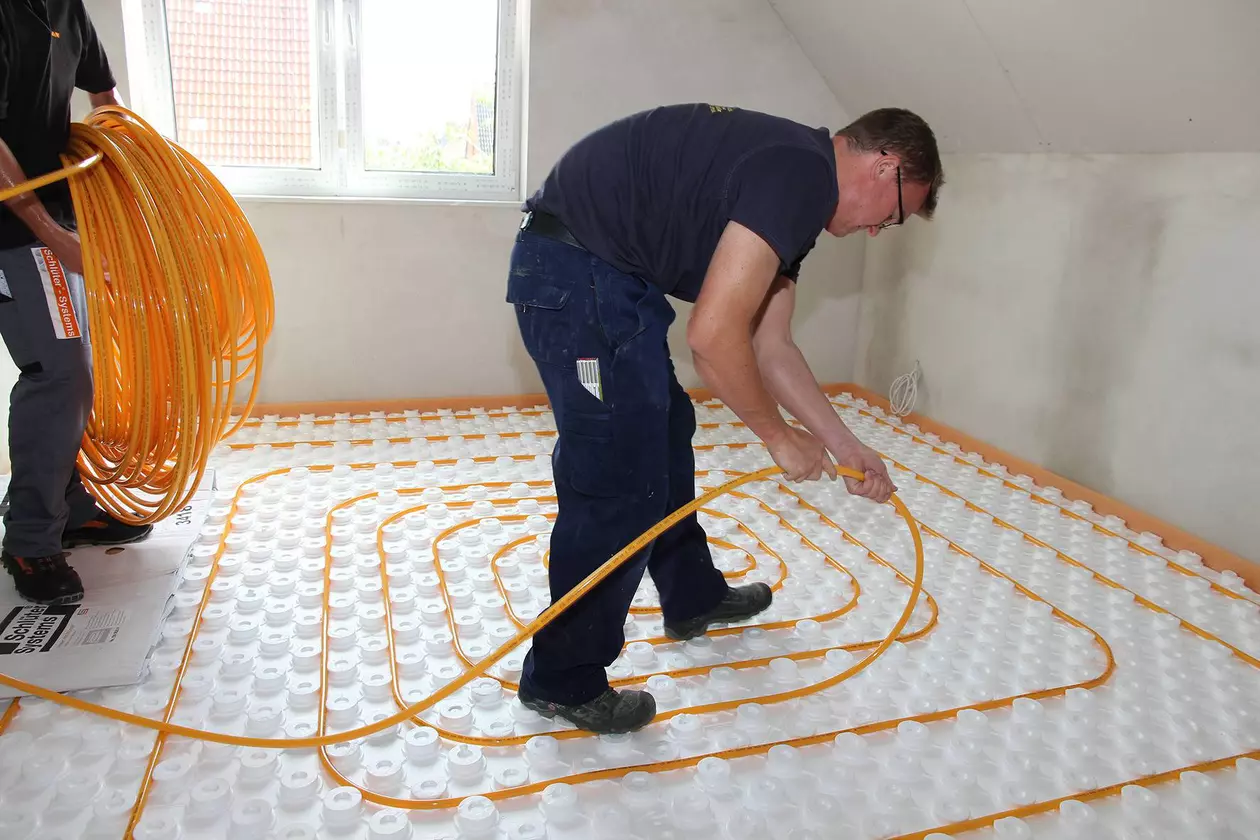 Un artisan applicateur pose les tuyaux de chauffage sur un panneau &agrave; plots BEKOTEC &agrave; l'&eacute;tage sup&eacute;rieur fra&icirc;chement cr&eacute;pi d'un nouveau b&acirc;timent
