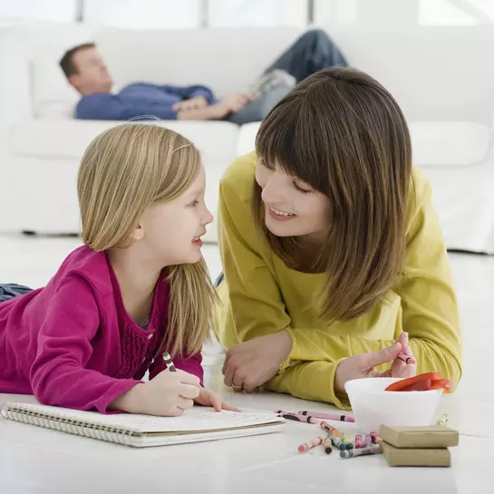 Moeder en dochter liggen v&oacute;&oacute;r een witte bank op de verwarmde tegelvloer en schilderen.