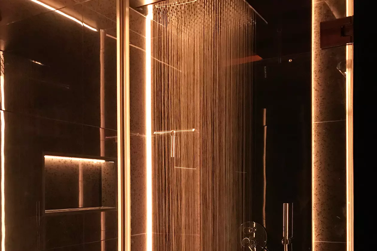 Dunkel geflieste Regendusche mit warm beleuchteter Lichtlinie und Nische