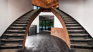 Beleuchtete, in einem Bogen geschwungene Doppeltreppe, die rechts und links in einem Atrium in die obere Etage f&uuml;hrt