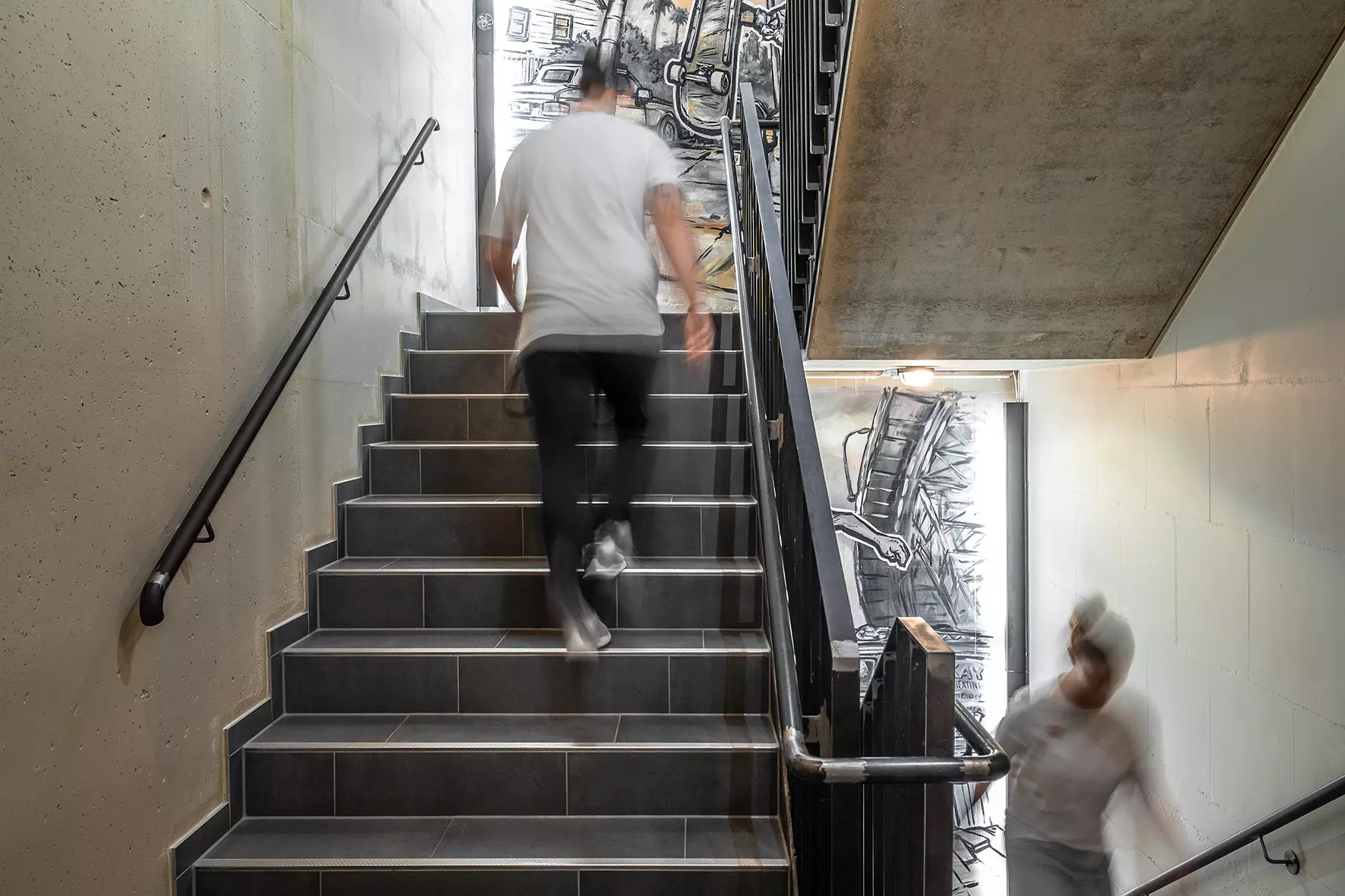 A man and a woman walk up the stairs, one behind the other, in a colourfully decorated hotel stairwell