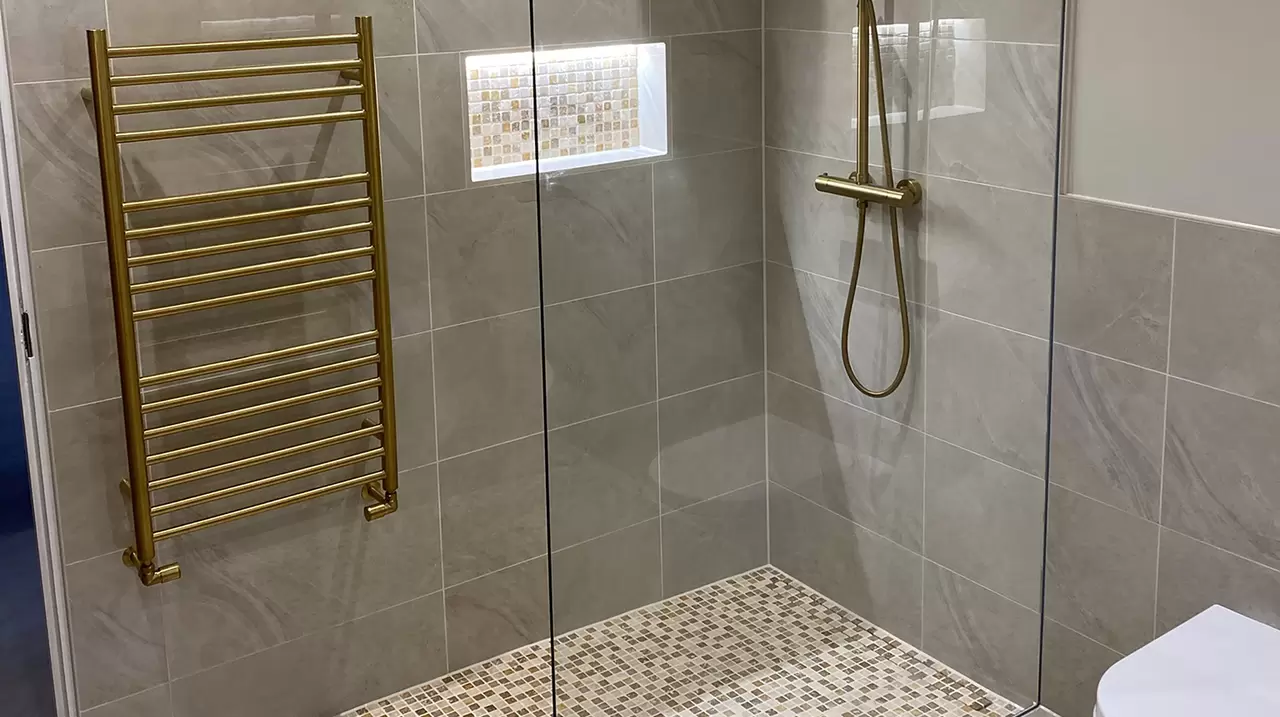 Douche &agrave; l'italienne avec sol en mosa&iuml;que, niche murale assortie, radiateurs et robinetterie de douche dor&eacute;s.