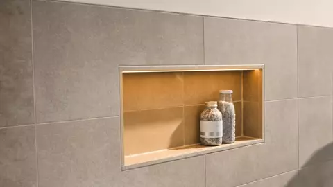 Illuminated niche in a light grey tiled wall with two bottles of bath salts