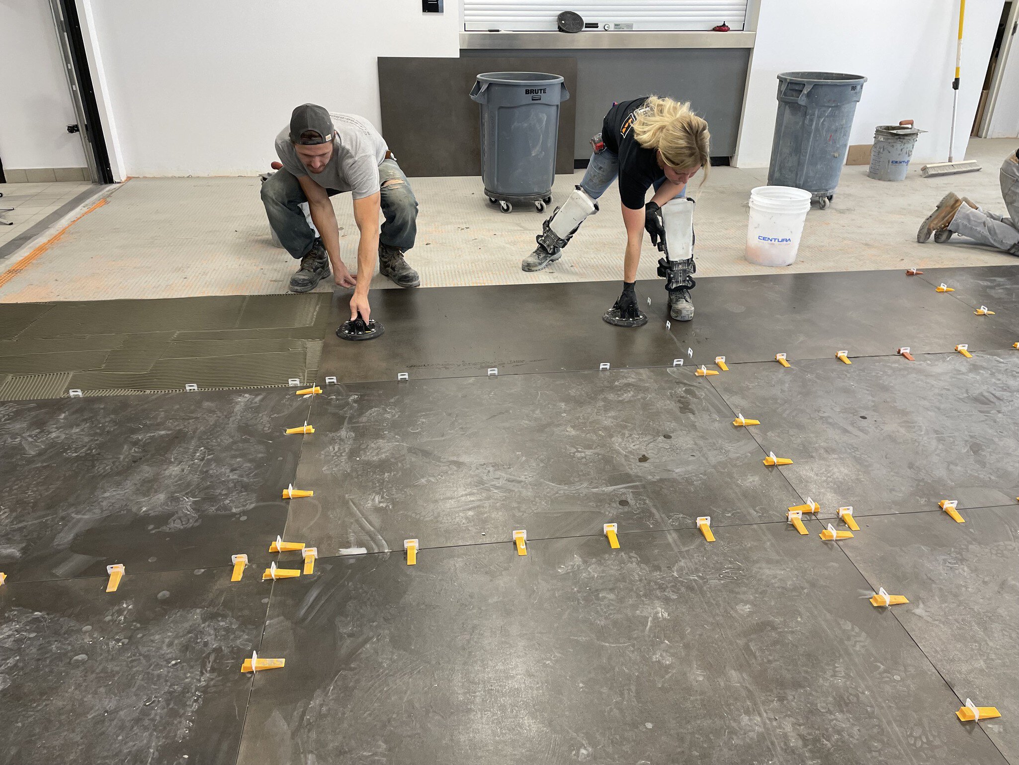 Deux installateurs posent des carreaux sur le sol de la salle d'exposition Lamborghini Montréal.