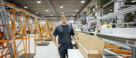 Auszubildender steht in ausgeleuchteter Logistik-Halle, an seinem Arbeitsplatz