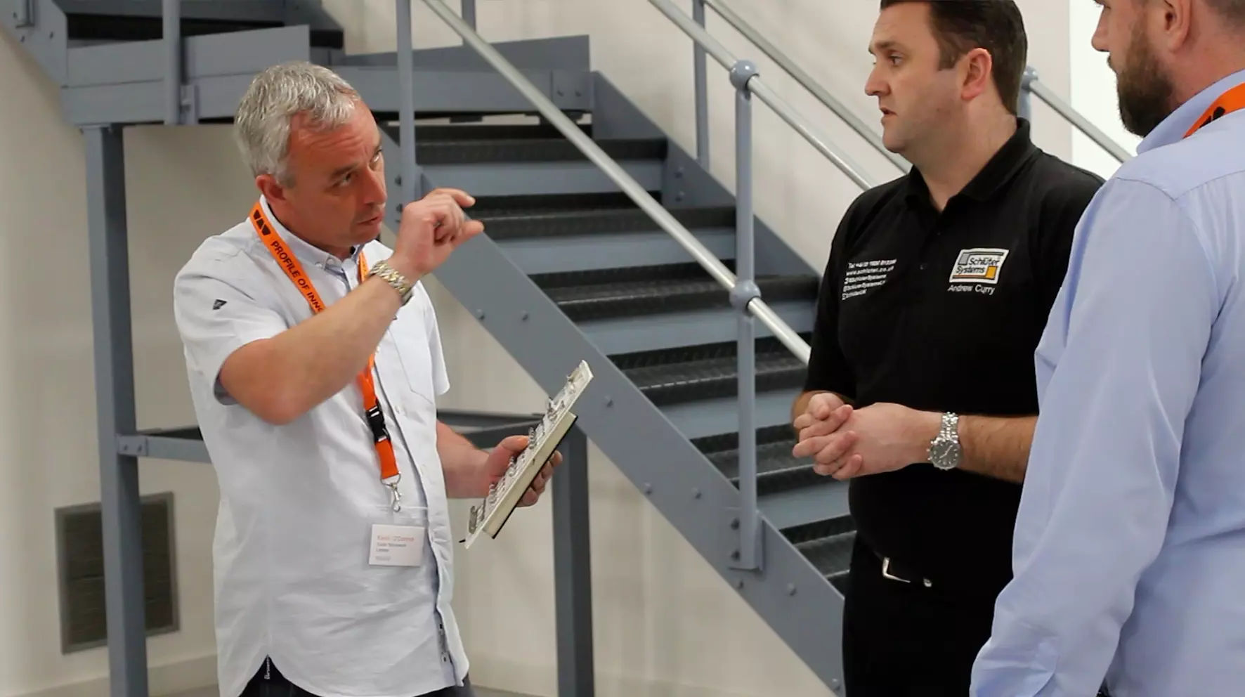 Three men pictured, one holding a sample of Schl&uuml;ter product, are in discussion